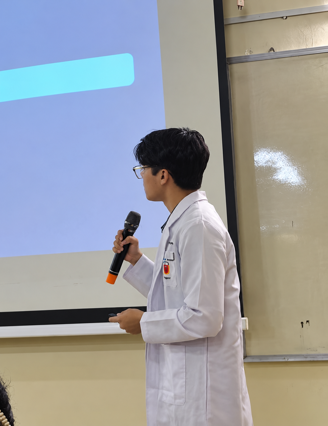Htet Myat Aung presenting in a classroom, wearing his medical-school coat